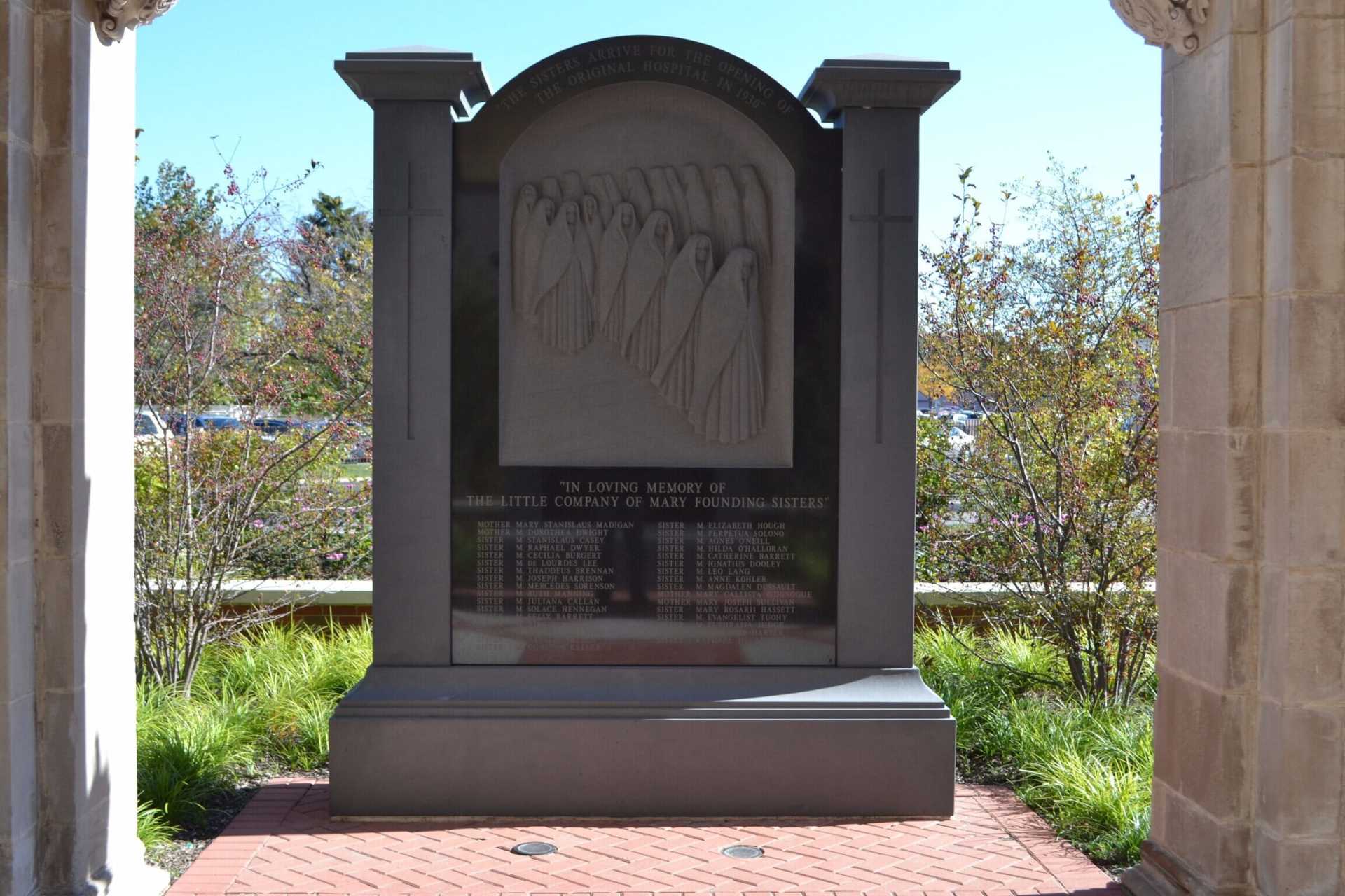 Memorial with carvings, beneath an archway. Dark stone structure with names inscribed on a plaque.