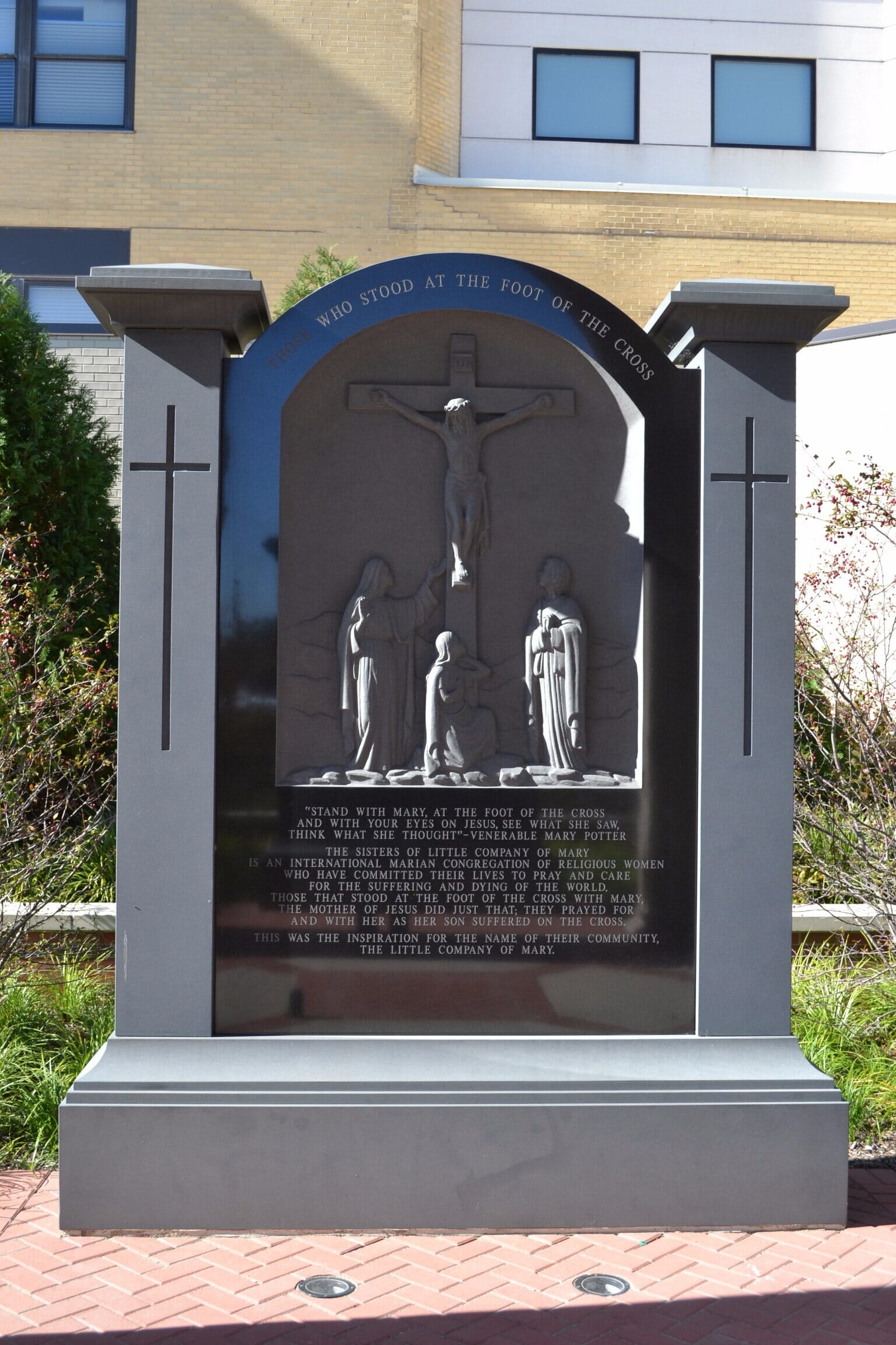 A black granite monument with a carved crucifixion scene, flanked by gray pillars.