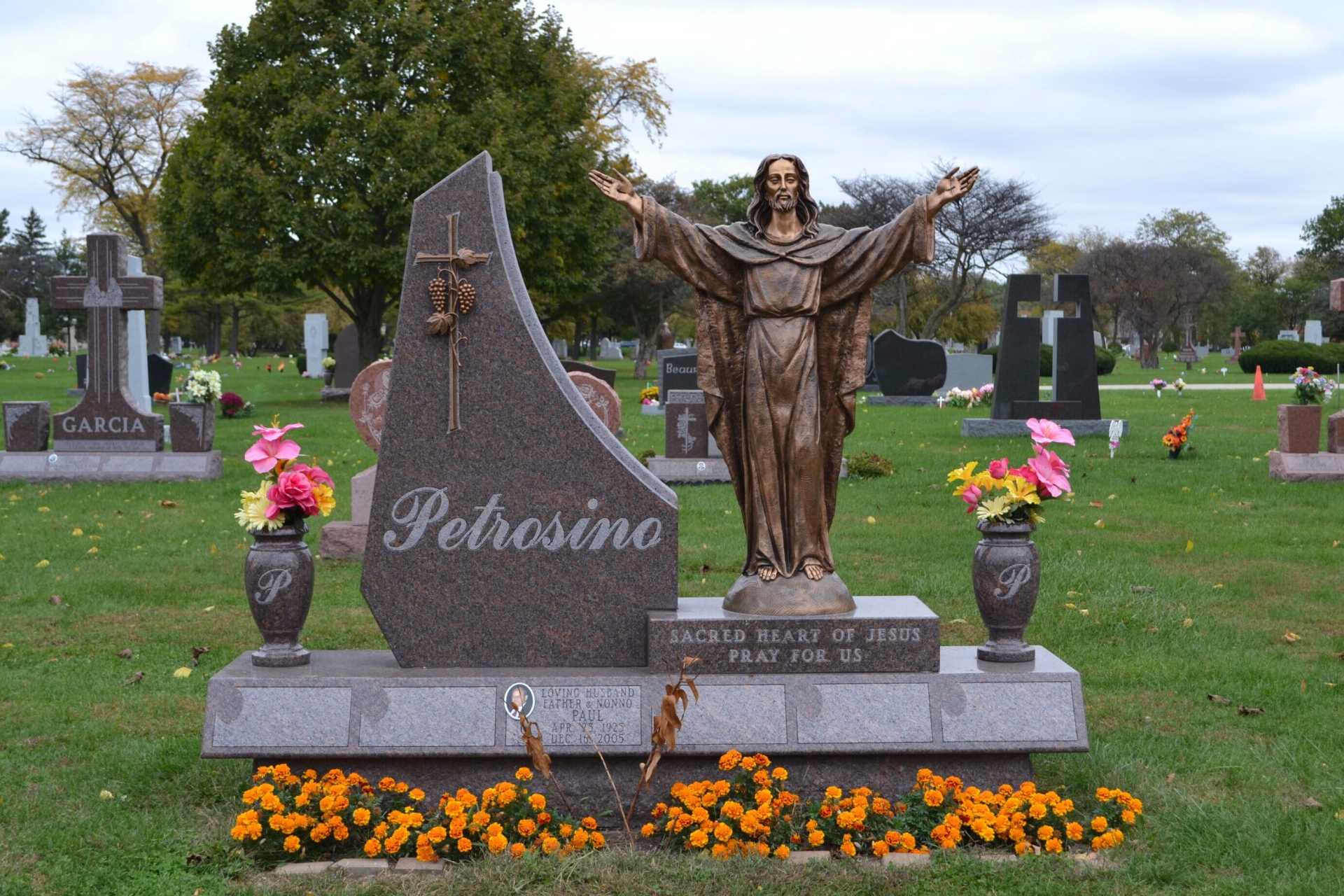 Grave with a bronze statue of Jesus with outstretched arms, next to a tilted headstone that reads 