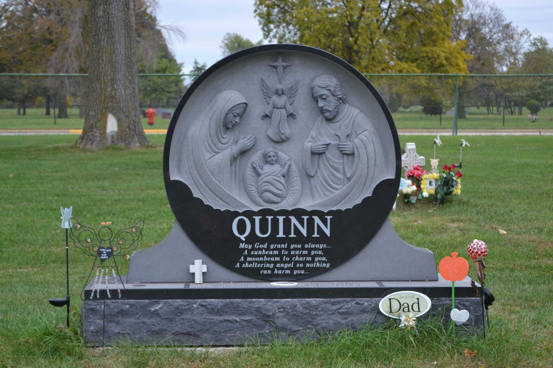 A tombstone with religious carving, including Mary, Joseph, and baby Jesus, in a cemetery.