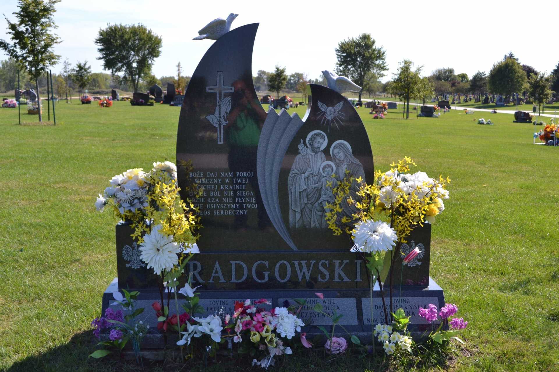 Headstone in a cemetery with flowers. Black monument with doves, religious images, and the last name 