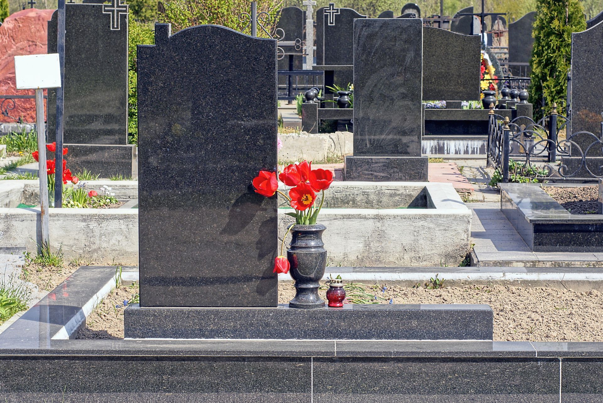 A black marble vase with red flowers at a granite monument on a grave in a cemetery.