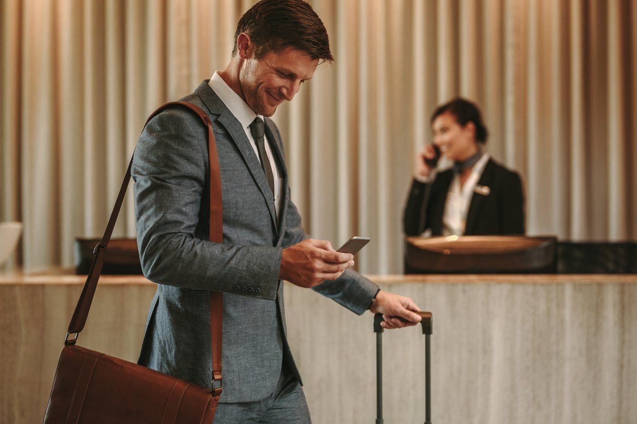 Hospitality industry concept - businessman checking his mobile phone while checking in in a hotel.