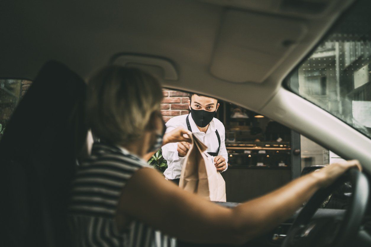 Man working in the restaurant industry, handing out a to-go dinner to a female consumer - curbside pickup concept.