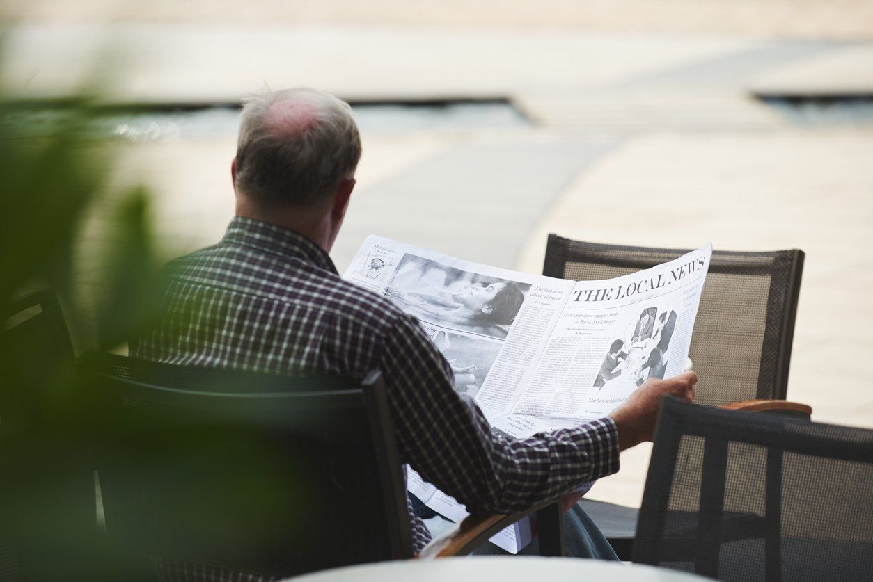 Unrecognized man reading local newspapers during a time of digitization.