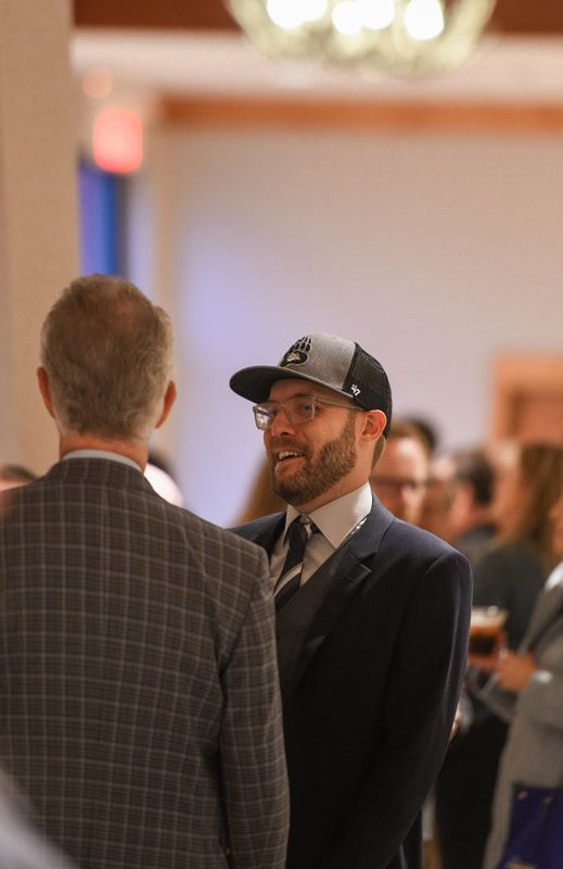 A man in a suit and hat is talking to another man.