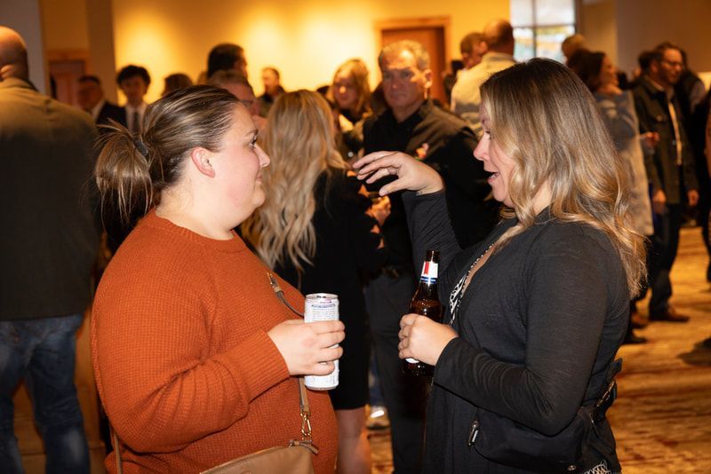Two women are talking to each other in a crowded room while holding drinks.