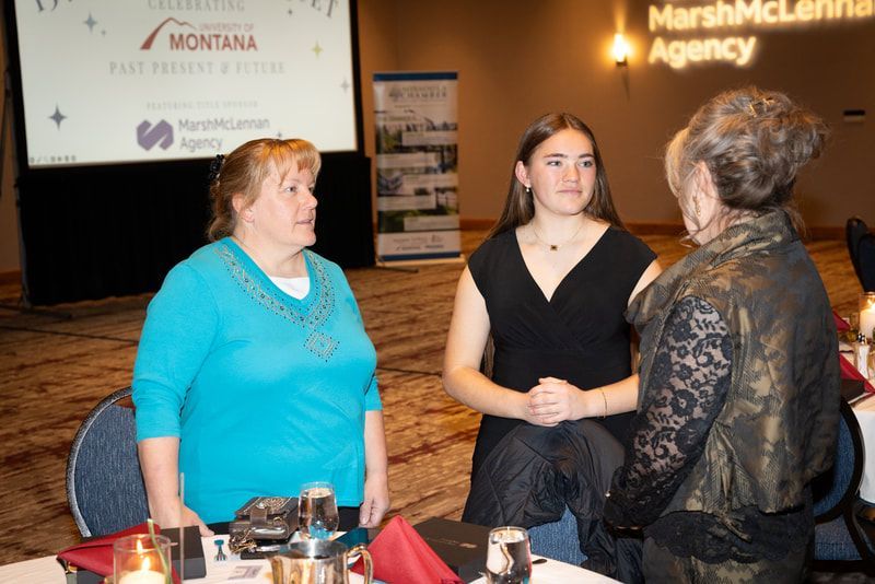 Three women are sitting at a table in front of a montana agency sign