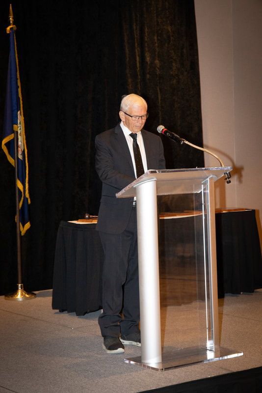 A man in a suit and tie is standing at a podium speaking into a microphone.