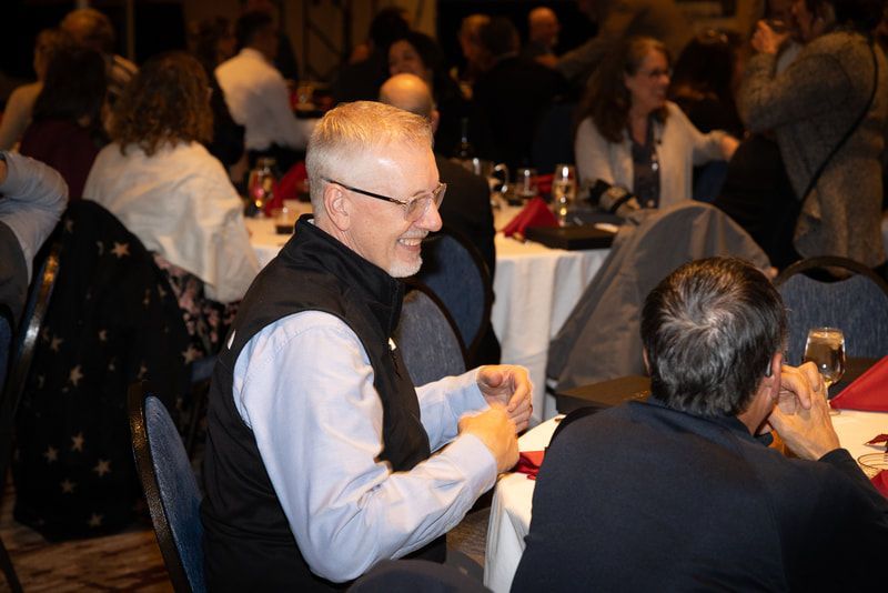 A man with glasses is sitting at a table with other people.