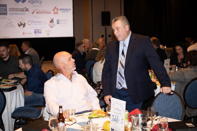 A man in a suit and tie is standing in front of a group of people sitting at tables.