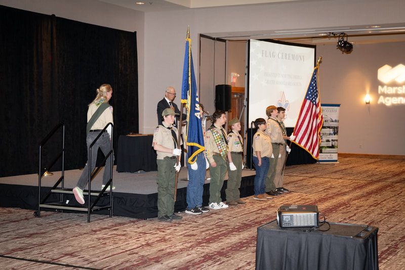 A group of boy scouts are standing on a stage holding flags.