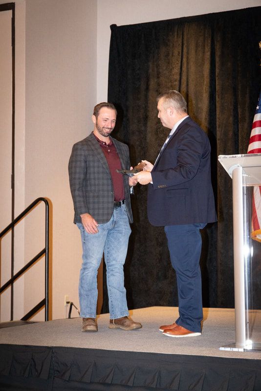 Two men are standing on a stage shaking hands.