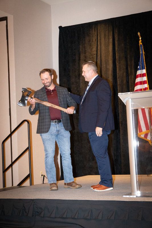 Two men are standing on a stage holding axes.