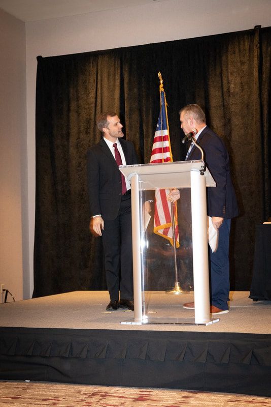Two men standing at a podium with an american flag in the background