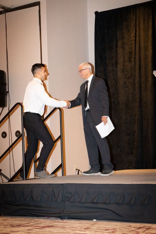 Two men are shaking hands on a stage in a room.