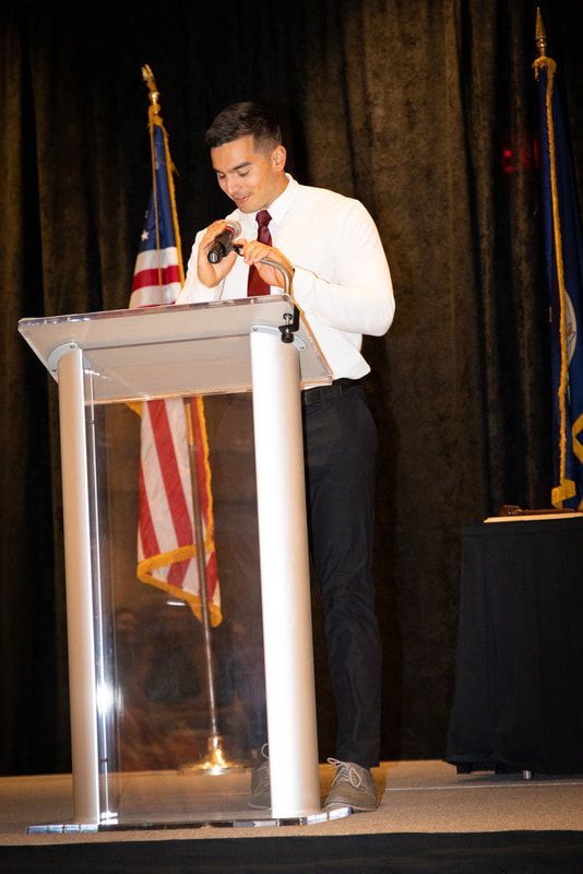A man is standing at a podium holding a microphone.