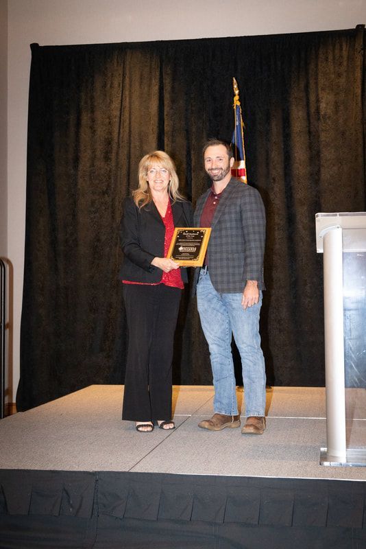 A man and a woman are standing on a stage holding a plaque.