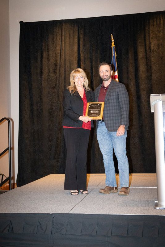 A man and a woman are standing on a stage holding a plaque.