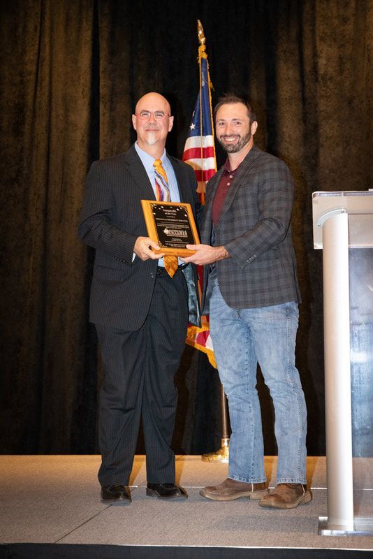 Two men are standing on a stage holding a plaque.