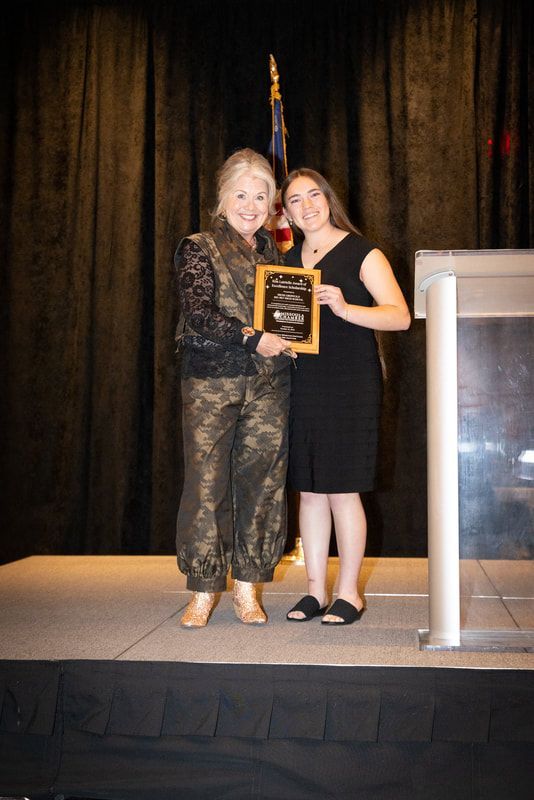 Two women are standing on a stage holding a plaque.