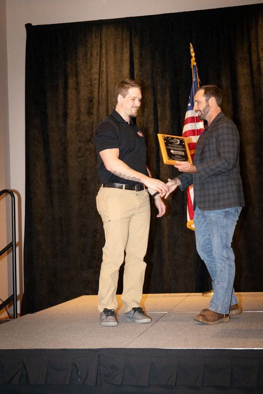 Two men are shaking hands on a stage with an american flag in the background.