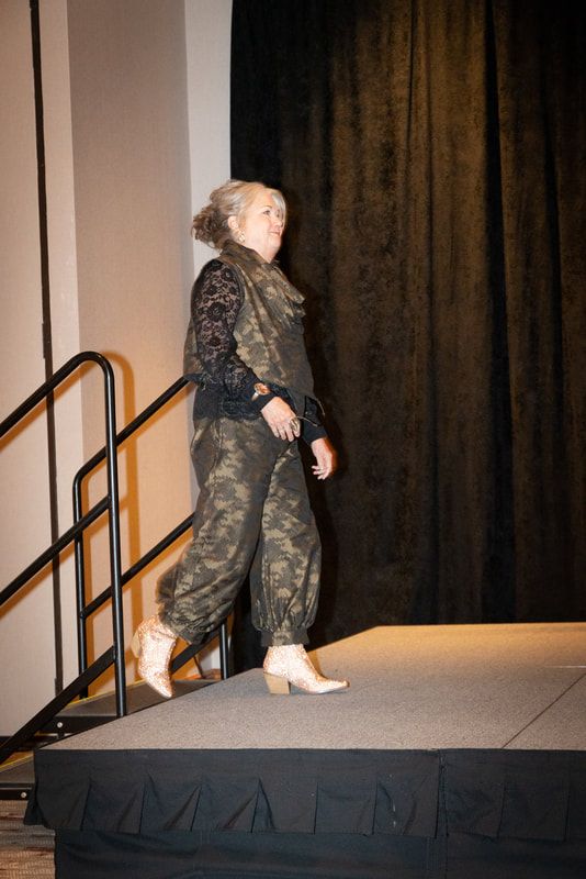 A woman is walking down a stage with a black curtain behind her.
