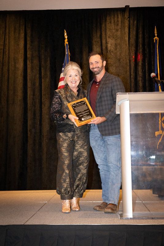 A man and a woman are standing on a stage holding a plaque.