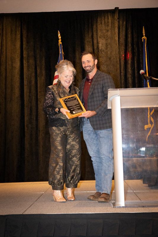 A man and a woman are standing on a stage holding a plaque.