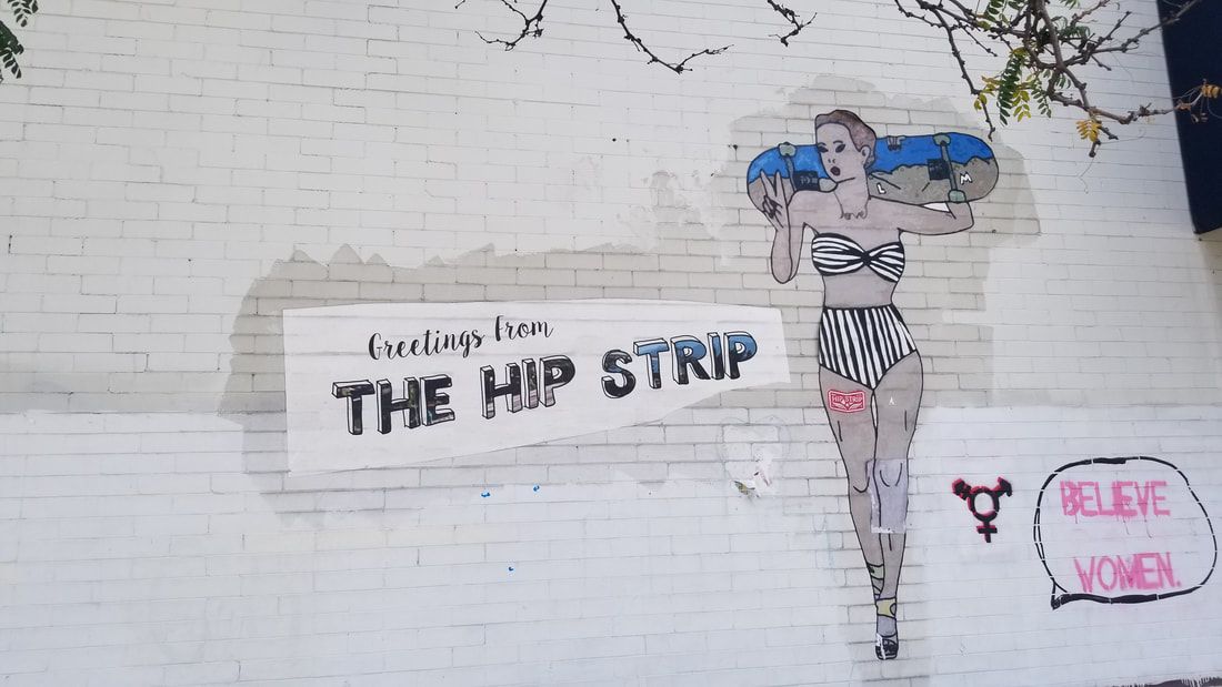 A woman in a bikini is holding a skateboard and a sign that says the hip strip
