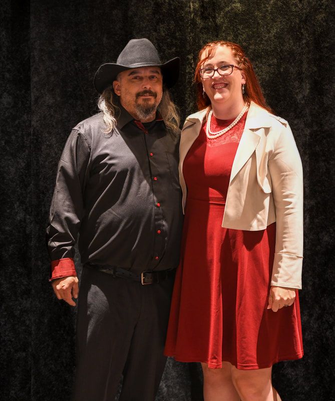 A man in a cowboy hat and a woman in a red dress are posing for a picture.