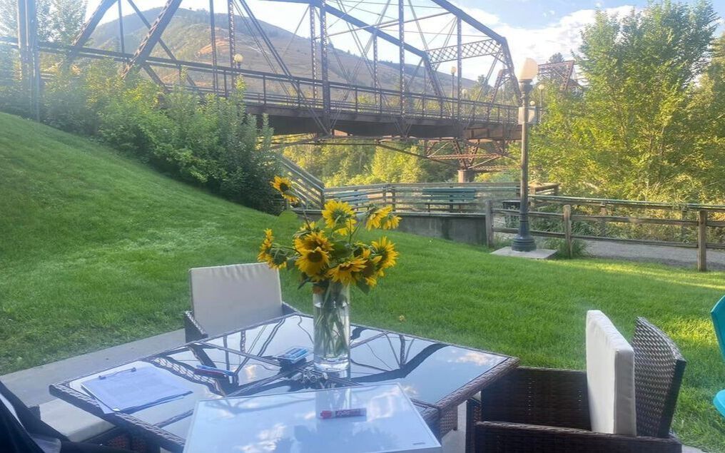 A table with a vase of sunflowers on it in front of a bridge.
