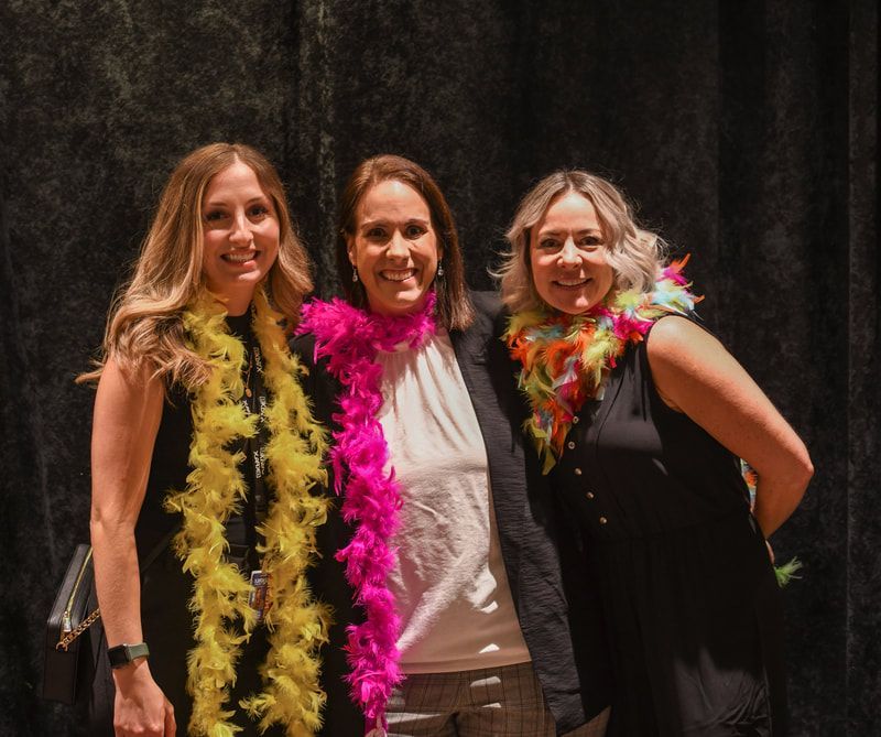 Three women are posing for a picture with feather boa around their necks.