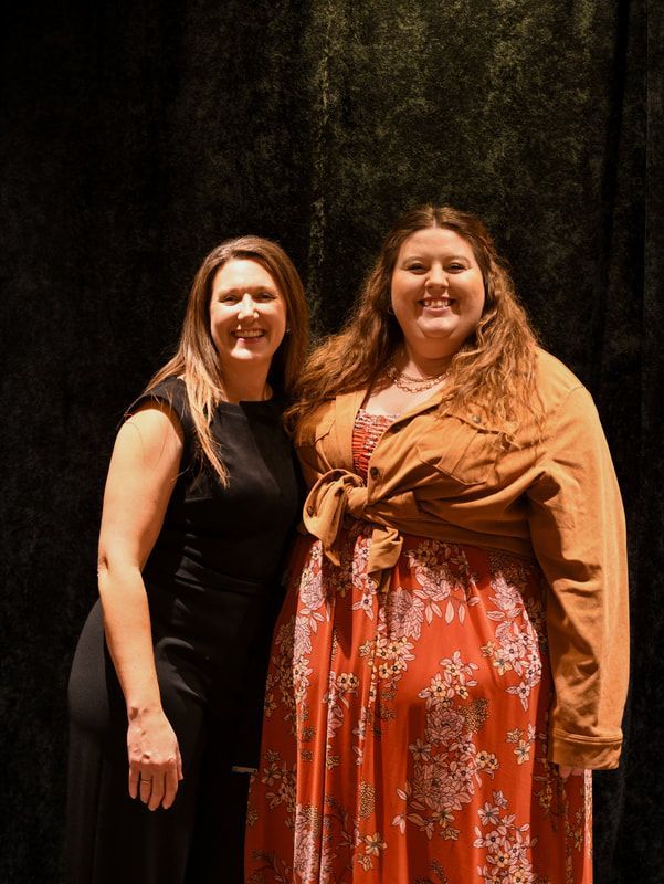 Two women are posing for a picture together in front of a black curtain.