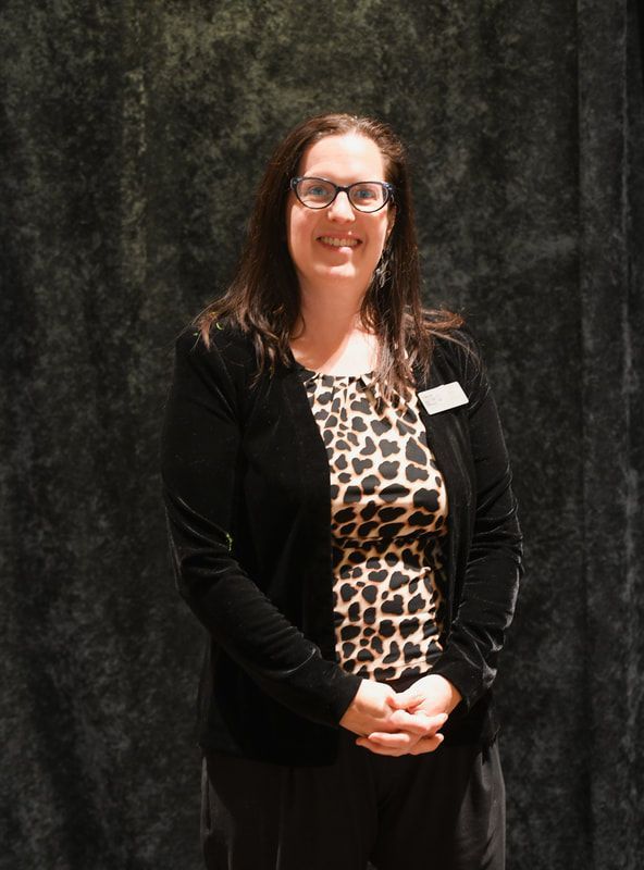 A woman wearing glasses and a leopard print shirt is standing in front of a black curtain