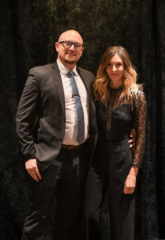 A man in a suit and tie is standing next to a woman in a black dress.