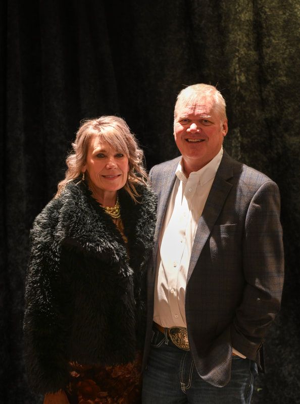 A man and a woman are posing for a picture in front of a black curtain.