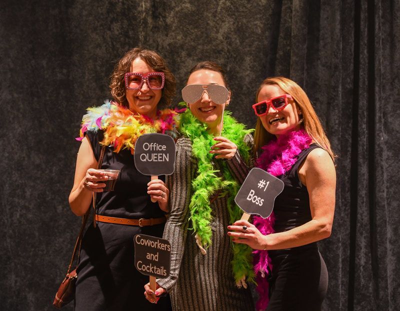 Three women are posing for a picture in a photo booth holding signs.