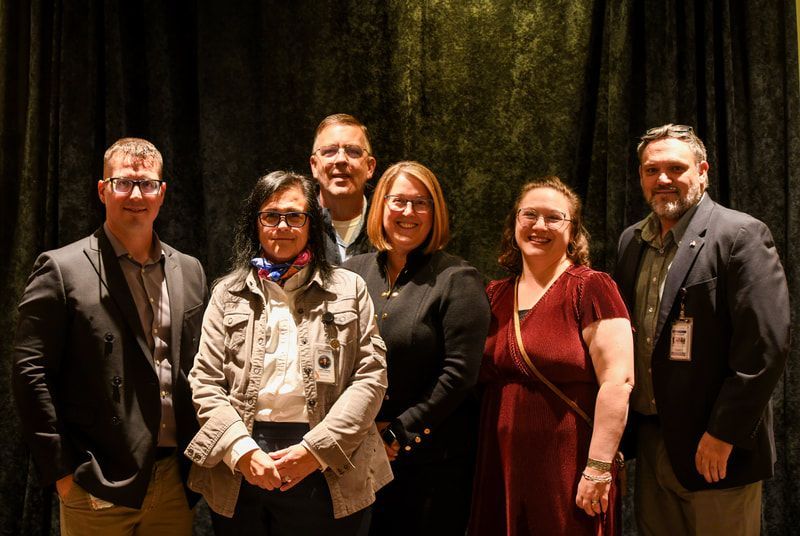 A group of people are posing for a picture in front of a black curtain.
