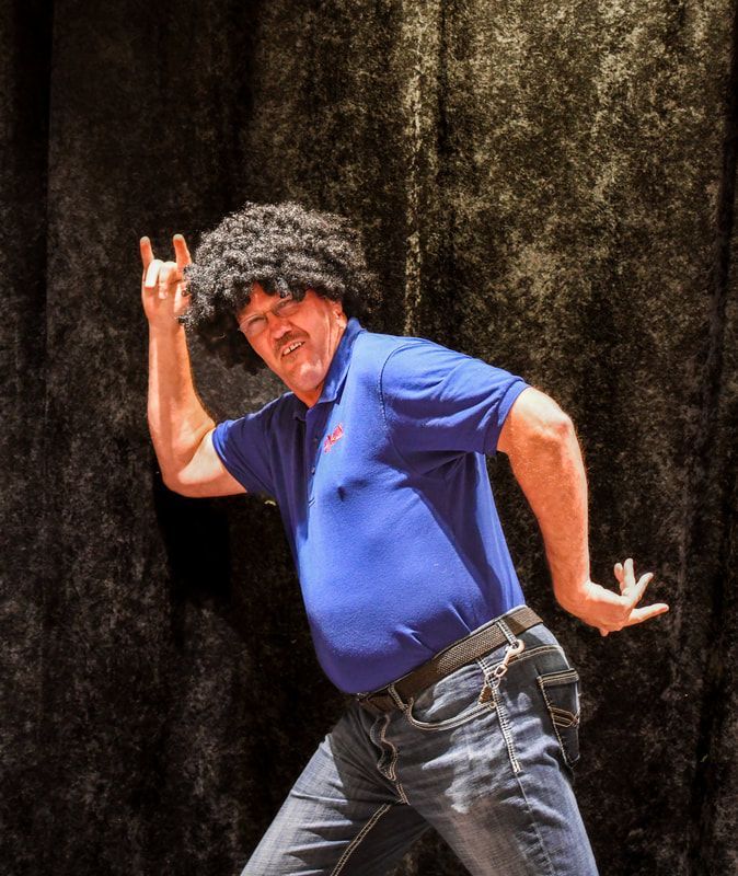 A man wearing a wig and a blue shirt is dancing