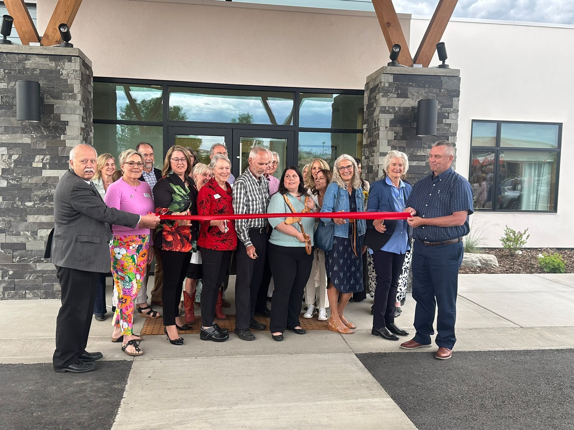 A group of people are cutting a red ribbon in front of a building.