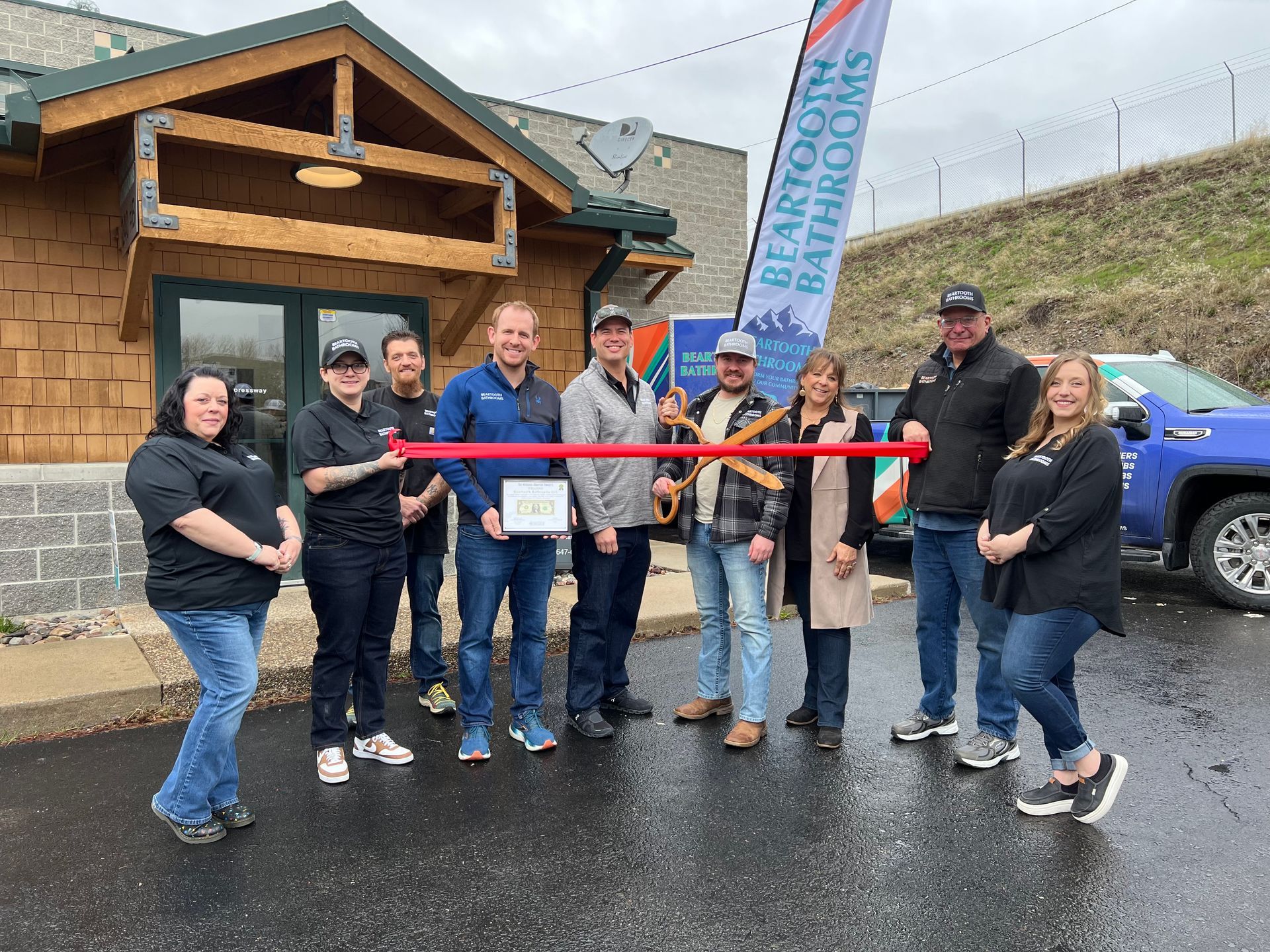 A group of people are standing in front of a building holding a red ribbon.