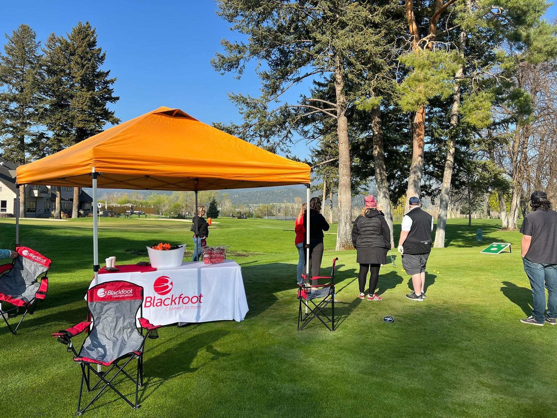 A group of people are standing under an orange tent in a grassy field.