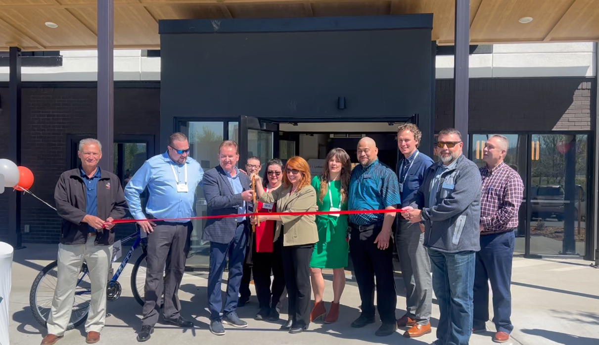 A group of people are cutting a red ribbon in front of a building.