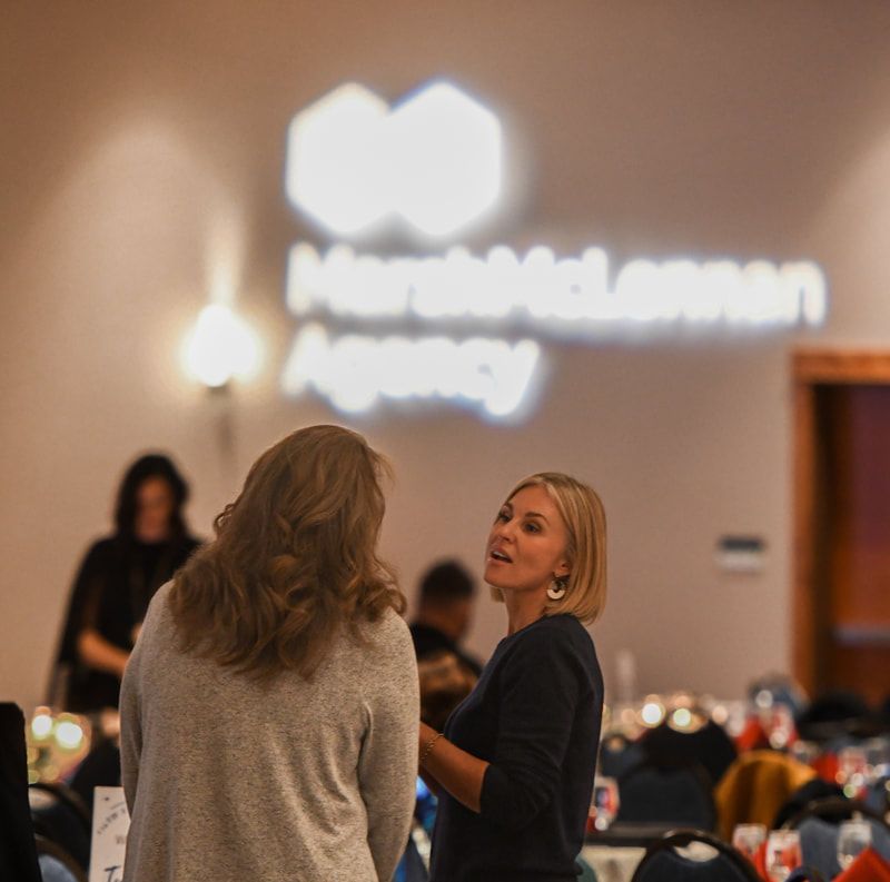 Two women are talking in front of a sign that says mcdonald agency