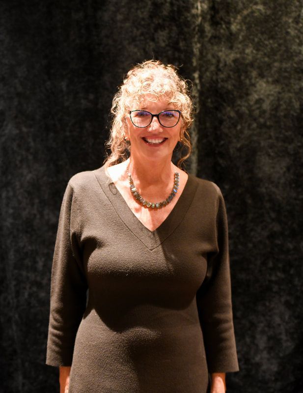 A woman wearing glasses and a black dress smiles for the camera