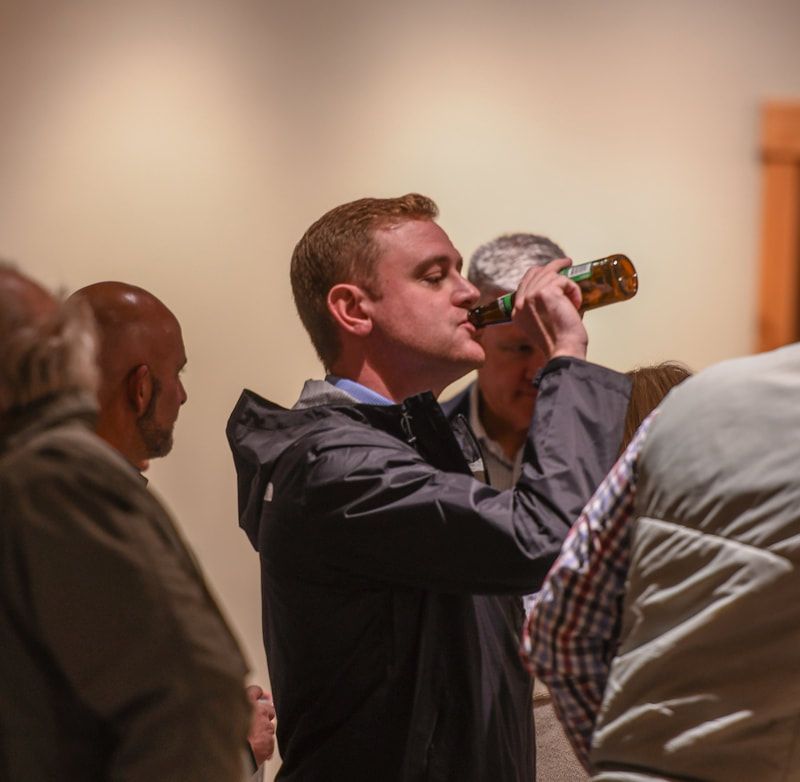 A man in a black jacket is drinking from a bottle