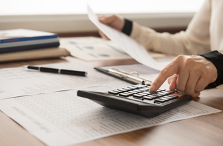 A person is using a calculator while holding a piece of paper.