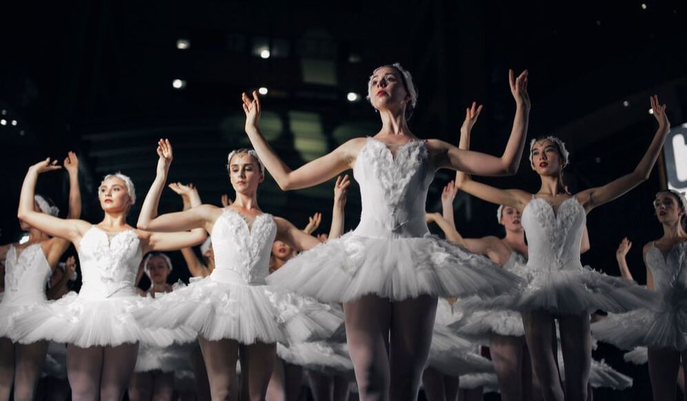 A group of ballerinas in white tutus are dancing on a stage.