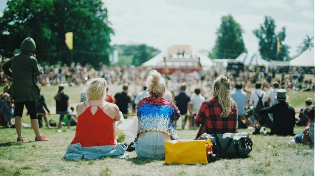 A group of people are sitting in the grass at a music festival.